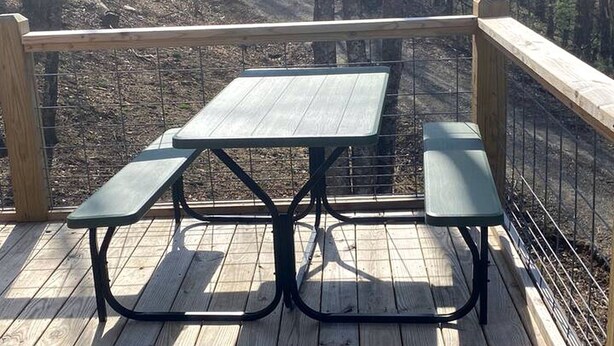 A picnic table with benches on a wooden deck with a metal railing.
