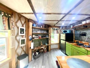 A compact kitchen with a refrigerator, sink, and wooden shelves.