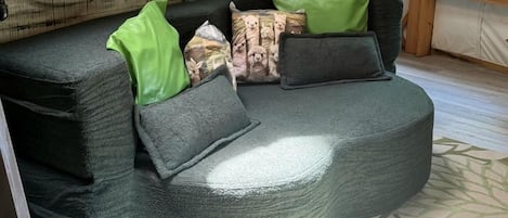 A cozy room with a curved sofa, a green door, and a window with a view of trees.