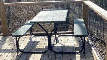 A picnic table with benches on a wooden deck with a metal railing.