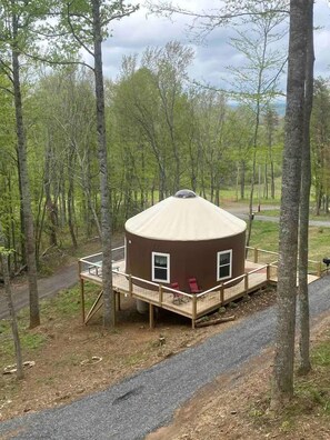 A small, brown, dome-shaped cabin with a wooden deck and two windows, surrounded by trees. - Mother Nature Glamping Getaway in a Countryside Yurt near Fancy Gap (Fancy Gap)
