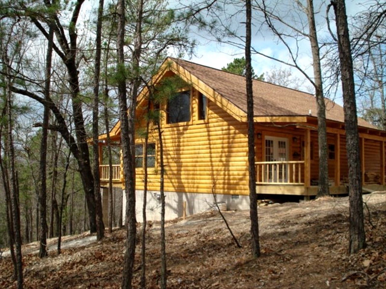 A log cabin with a porch, surrounded by trees.