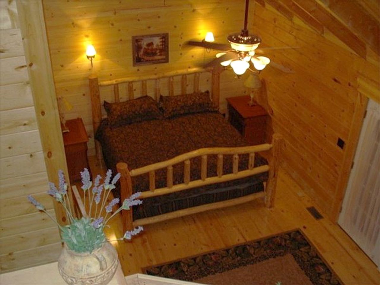 Een houten slaapkamer met een bed, twee nachtkastjes, een hanglamp en een lijst met een foto aan de muur.