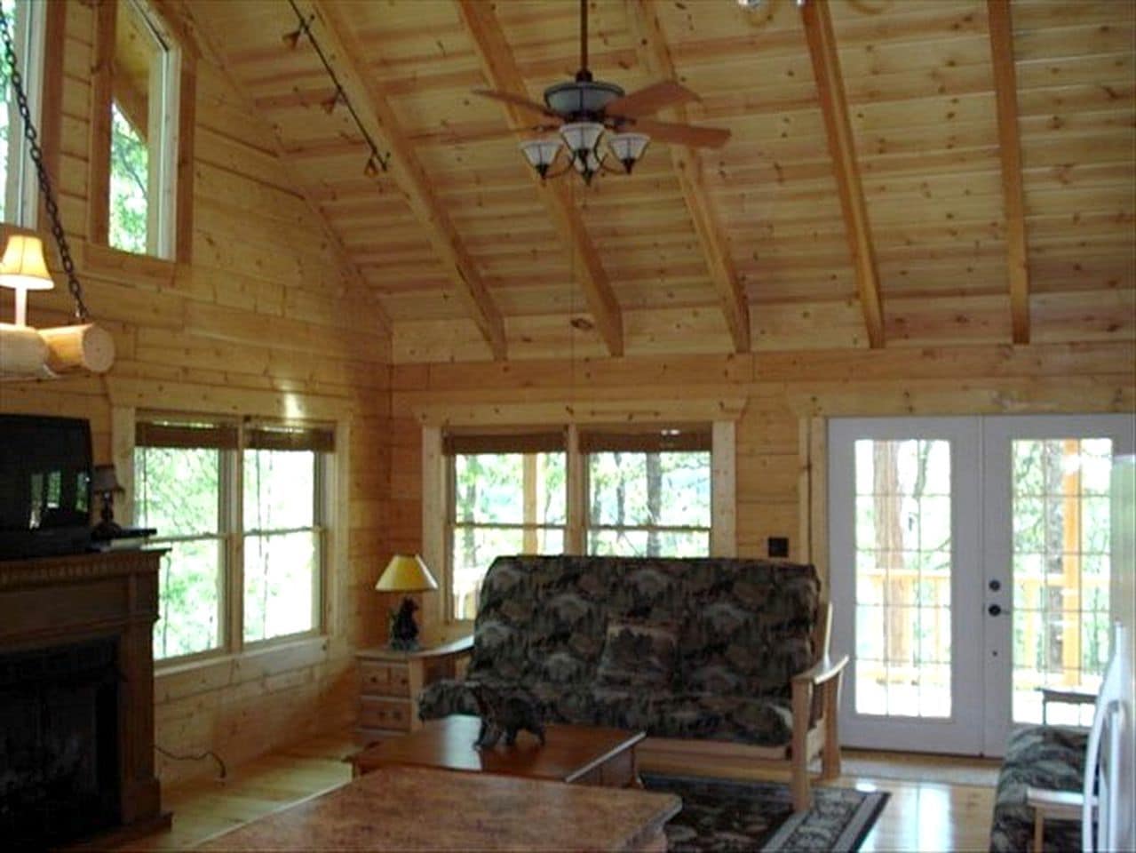 L’intérieur d’une cabane en rondins, avec une cheminée, un canapé, une table à manger et un ventilateur de plafond.