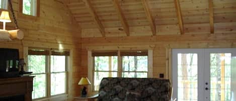 L’intérieur d’une cabane en rondins, avec une cheminée, un canapé, une table à manger et un ventilateur de plafond.