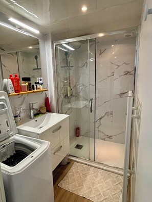 Casa de banho moderna com chuveiro em cabine de vidro, lavatório branco e espelho em cima.