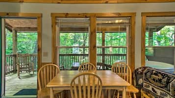 A wooden dining table with six chairs, large windows with a view of a forest, and a wooden bench with a patterned cushion.