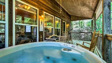 Ein Whirlpool in einer Holzhütte mit einer Veranda, großen Fenstern und Blick auf den umliegenden Wald.