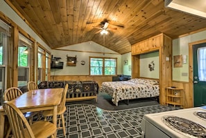 Ein Interieur einer Hütte mit Essbereich, einer Couch, einem Bett und einer Küche.
