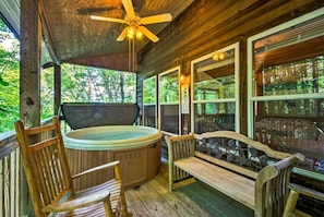 Eine Holzterrasse mit Whirlpool, Holzstühlen, einer Bank und großen Fenstern mit Blick auf einen Wald.