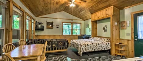 A cabin interior with a dining area, a sofa, a bed, and a kitchen.