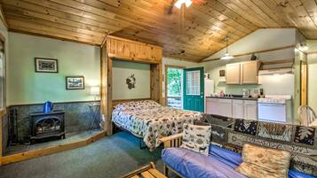 A cozy cabin interior with a bed, sofa, wooden ceiling, and a kitchenette.