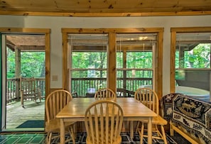 Ein Holzespeise Tisch mit sechs Stühlen, große Fenster mit Blick auf einen Wald und eine Holzbank mit gemustertem Kissen.