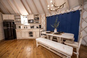 A rustic kitchen with wooden cabinets, a black refrigerator, a dining table with plates, and a bench.