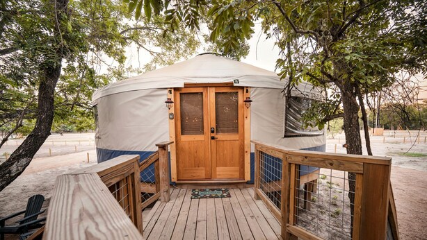 Una yurta con puerta de madera, una terraza con barandilla y un felpudo.