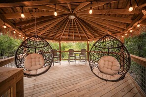 A wooden deck with hanging chairs and a thatched roof. - Enchanting Glamping Yurt with Access to the Tranquil Medina River in Bandera, Texas (Bandera)