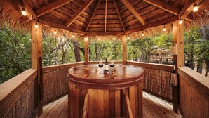 A wooden gazebo with a round table, a bottle of wine, and a glass on the table.