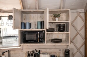 A kitchen with a Galanz microwave, wooden shelves with cups and bowls, a potted plant, and a Keurig coffee maker.