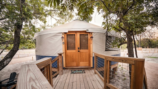 A yurt with a wooden door, a deck with a railing, and a welcome mat.