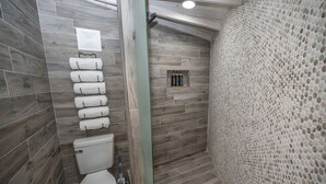 Un baño con suelo de madera, inodoro, zona de ducha y un perchero para toallas.