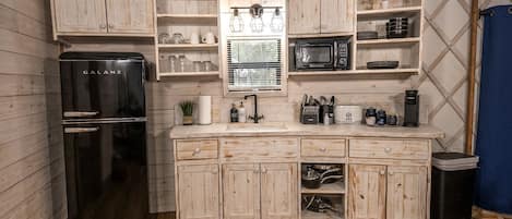 A compact kitchen with a black refrigerator, wooden cabinets, a microwave, and a sink.