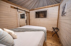 A wooden-paneled room with a bed, a window, and a door.