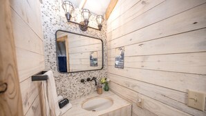 A wooden cabin bathroom with a sink, mirror, towel rack, and wall-mounted light fixture.