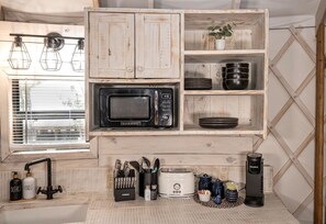 Una cocina compacta con un microondas Galanz, platos negros, una cafetera Keurig y un fregadero con lavavajilla.