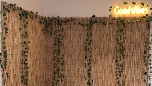 Ein Schlafzimmer mit einem Bett, Kissen, einem Nachttisch mit einer Vase sowie einer Wand mit Bambuspaneelen und Efeu.