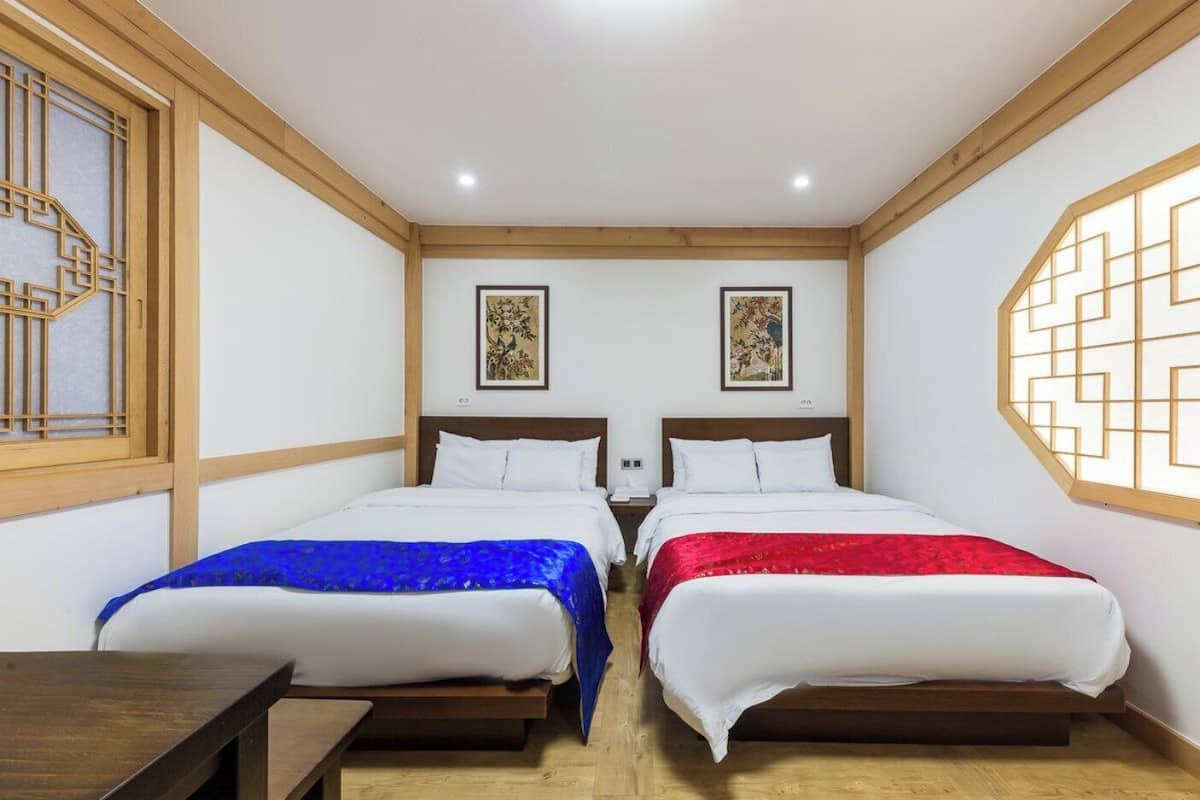 Una habitación con dos camas, un escritorio de madera y un panel decorativo en la pared.