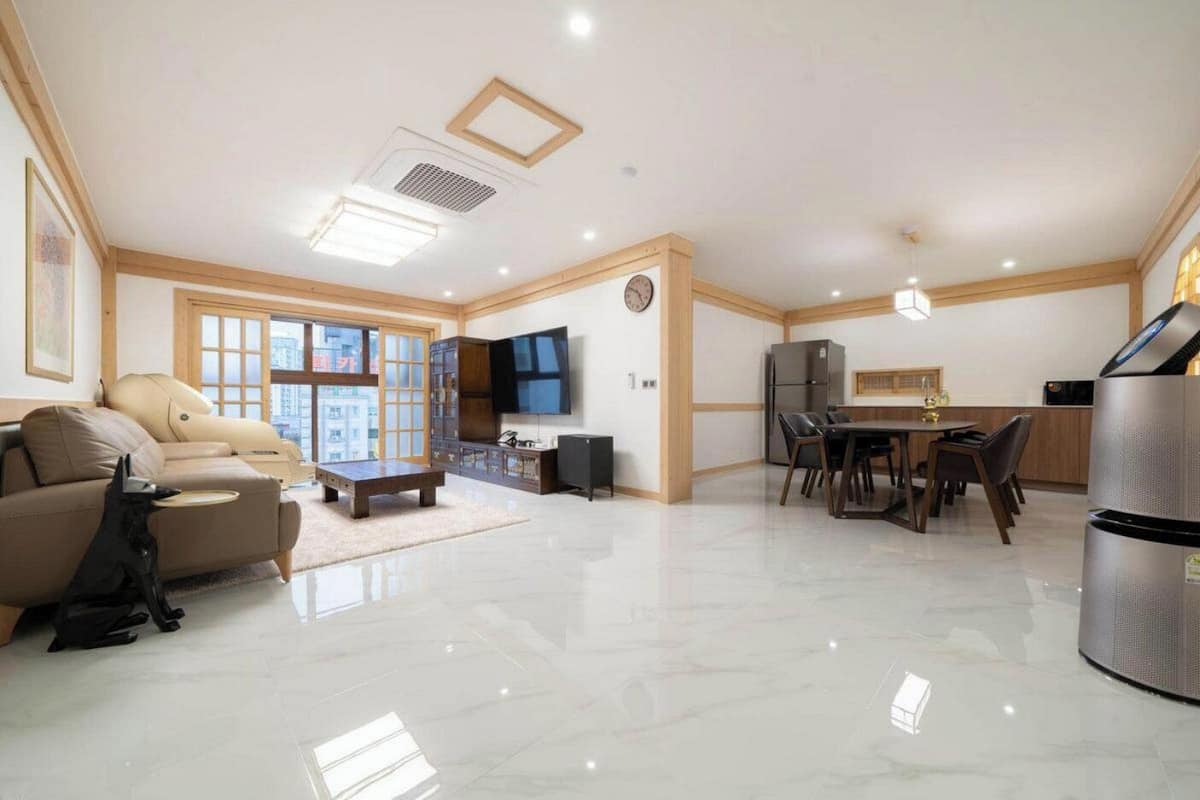 Amplia sala de estar con sofá, mesa de centro, televisor, mesa de comedor con sillas, área de cocina con refrigerador y un ventanal grande.