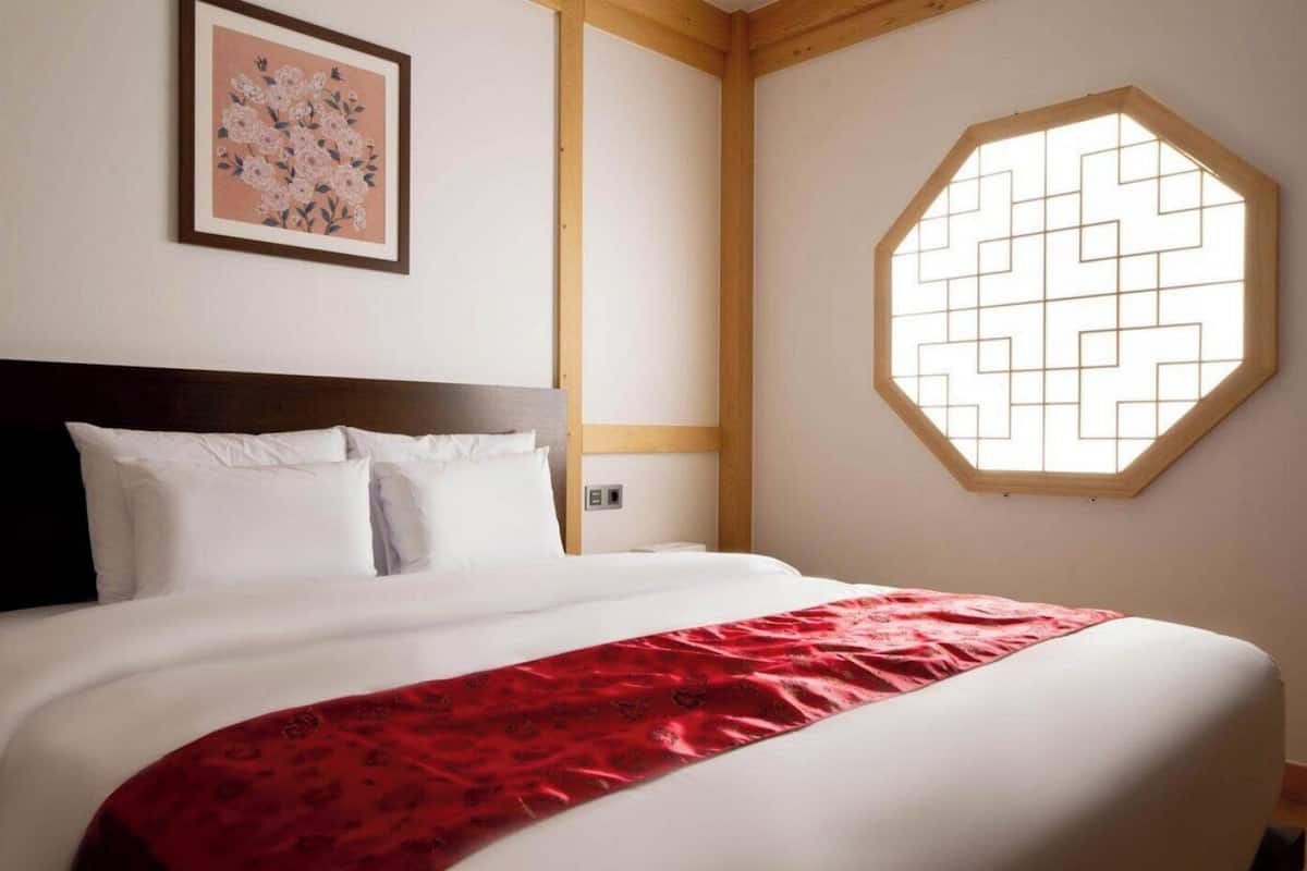 Una habitación de hotel con una cama, una obra de arte floral enmarco y un diseño de ventana geométrico.