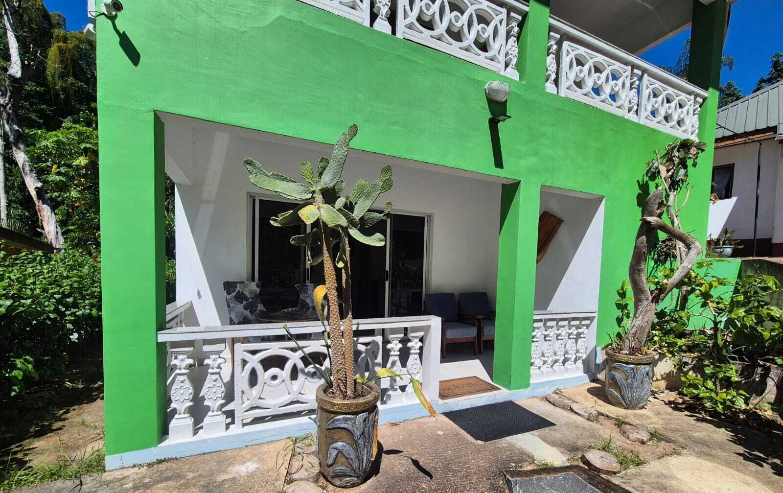 Un edificio de dos pisos con fachada verde, barandillas de balcón blancas y plantas en macetas.