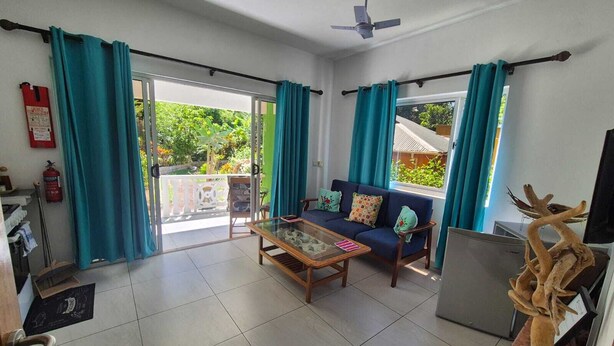 A living room with a sofa, coffee table, and curtains. - Fond B'offay Lodge (Praslin Island)