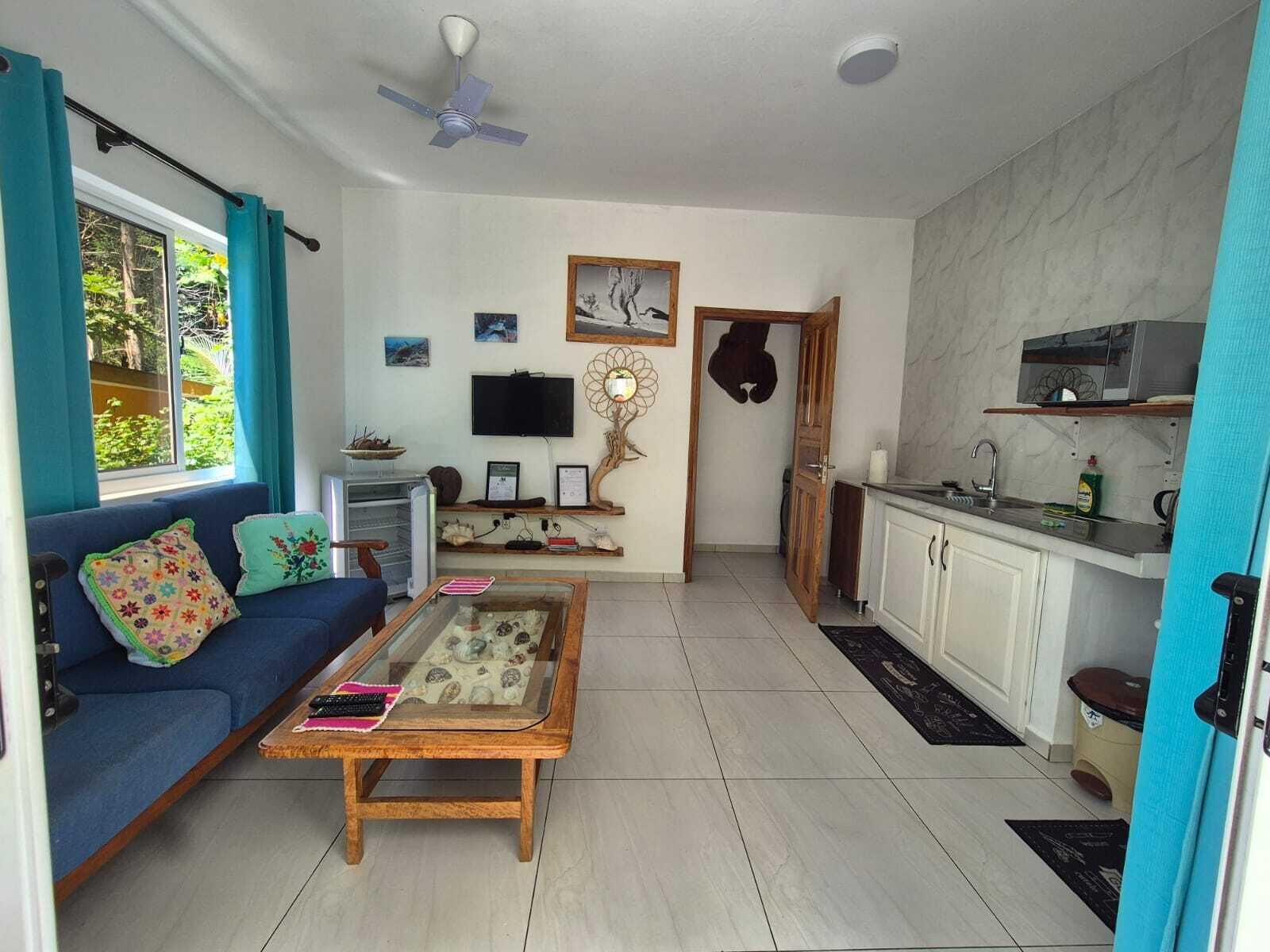 A living room with a sofa, coffee table, TV, and a kitchen area with cabinets and a sink.