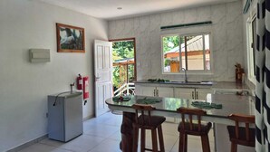 A kitchen with a marble backsplash, a refrigerator, a dining table with bar stools, and a window with a view of greenery. - Fond B'offay Lodge (Praslin Island)