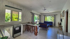 A kitchen with a gas stove, a dining area with a table and chairs, a blue sofa, and a ceiling fan. - Fond B'offay Lodge (Praslin Island)
