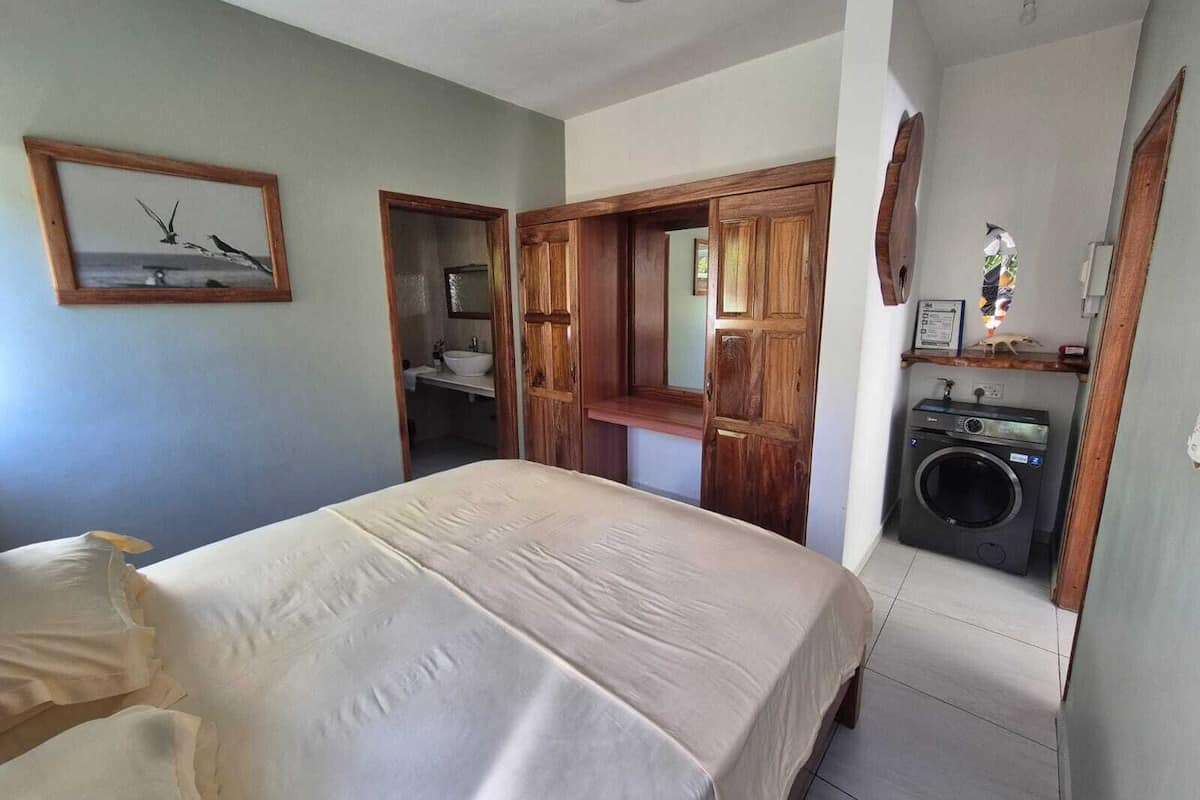 A bedroom with a bed, a wooden door leading to a bathroom, and a washing machine.