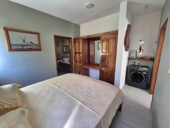A bedroom with a bed, a wooden door leading to a bathroom, and a washing machine.
