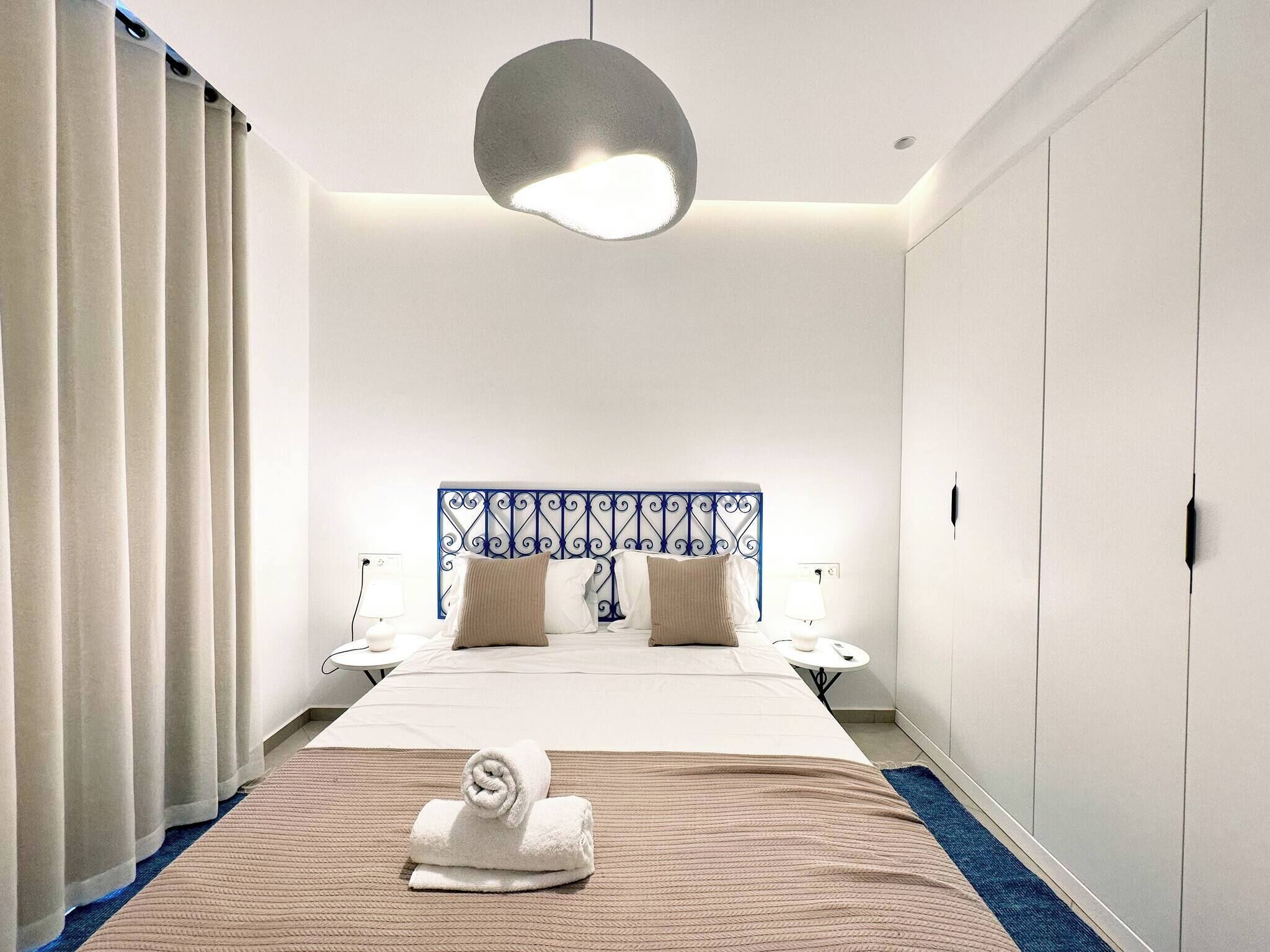 Une chambre d’hôtel avec un lit, une tête de lit, des tables de chevet, une serviette et un luminaire suspendu.