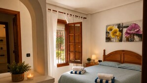 A bedroom with a bed, a nightstand, a bedside lamp, a window with curtains, a wall-mounted painting, and a potted plant. - Ground Floor in Playa Flamenca with Pool (Alicante)