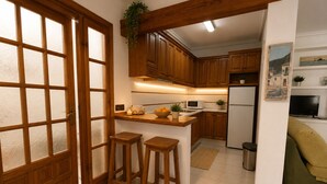A kitchen with wooden cabinets, a microwave, a refrigerator, and two stools. - Ground Floor in Playa Flamenca with Pool (Alicante)
