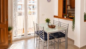 Een eethoek met een glazen tafel, metalen stoelen, een potplant en uitzicht door een kantgordijn.