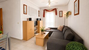 Een moderne woonkamer met een grijze bank, houten kasten, een televisie en een plafondventilator.