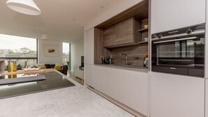 A modern kitchen with white cabinetry, a built-in oven, and a large window. - Designer Urban Apartment with City Terrace (Edinburgh)