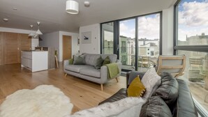 A modern apartment with a kitchen, grey sofa, leather couch, and large windows offering city views. - Designer Urban Apartment with City Terrace (Edinburgh)