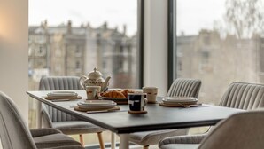 A dining table set with plates, a teapot, and croissants, with a city view through large windows. - Designer Urban Apartment with City Terrace (Edinburgh)