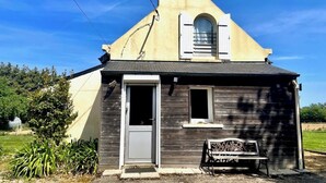 Um pequeno edifício térreo com telhado em duas águas, uma porta e uma pequena janela.