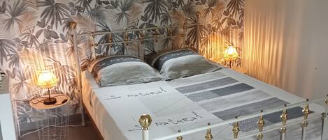 Un dormitorio con cama, mesita de noche, lámpara y ventana.