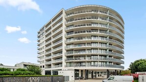 Un immeuble à plusieurs étages doté d’une façade incurvée, de balcons et d’un espace de stationnement.